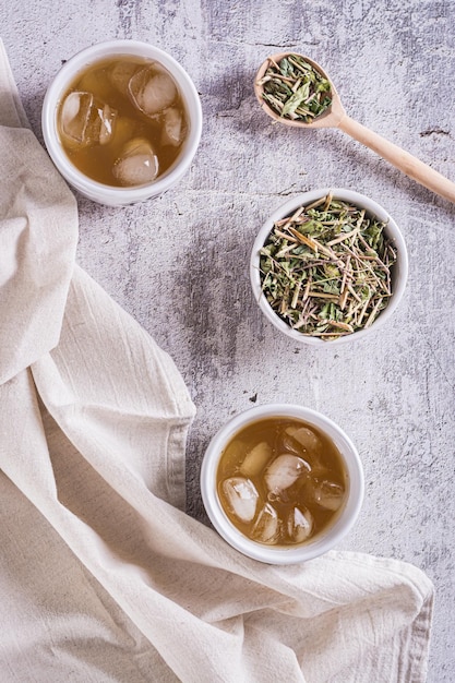 Iced green japanese hojicha tea in cups and leaves in a bowl on the table top and vertical view