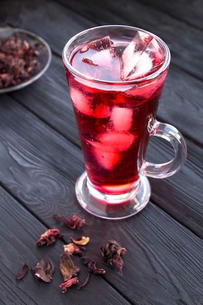 Iced hibiscus or karkade tea in the glass on the black wooden