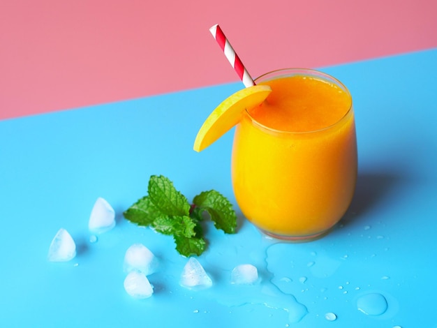 Iced mango smoothies glass on a pink and blue color background for summer drinks