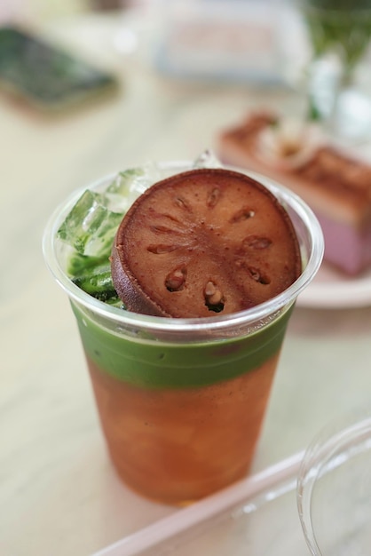 Iced matcha tea with Bael fruit juice topped sliced dry bael fruit in cafe background