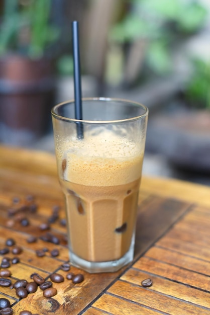 Iced milk espresso with coffee beans on wooden table closeup