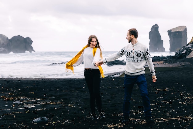 Icelandic tourist couple walking to the black sand beach south coast Happy woman and man visiting tourist attraction