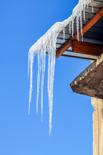 Icicles on the eaves of the house against the sky view from below Snow winter icicles