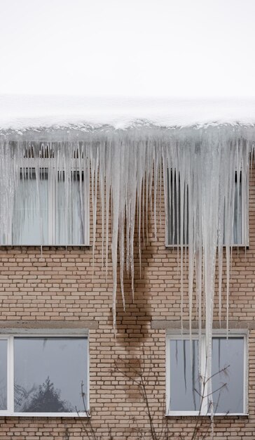 Icicles hang in front of the windows from the roof of a residential brick buildingDangerous for life