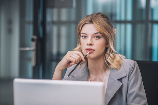 Idea, thoughts. Thinking beautiful business woman holding pencil near mouth sitting working at laptop in office