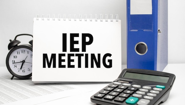 Iep meeting words on white notebook and calculator black vintage alarm clock and blue paper folder