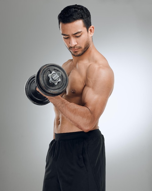 If you want to look good you have to lift heavy Shot of a man working out with weights while standing against a grey background