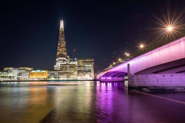 Photo illuminated bridge over river against buildings at night