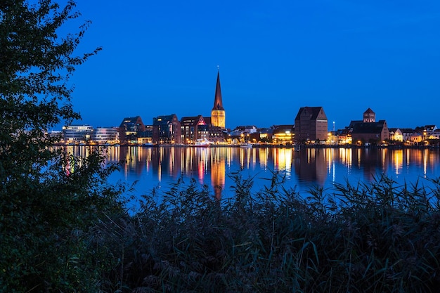 Photo illuminated buildings by lake against sky at dusk