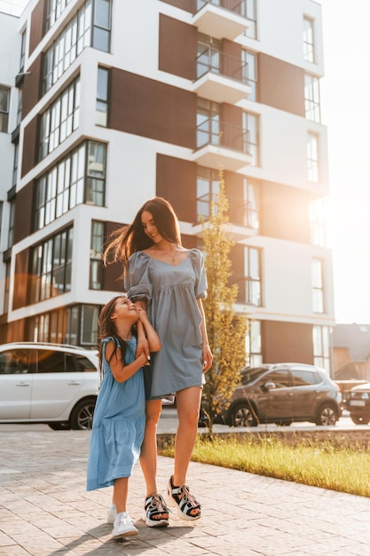 Illuminated by sunlight Young mother with her little daughter walking near the buildings