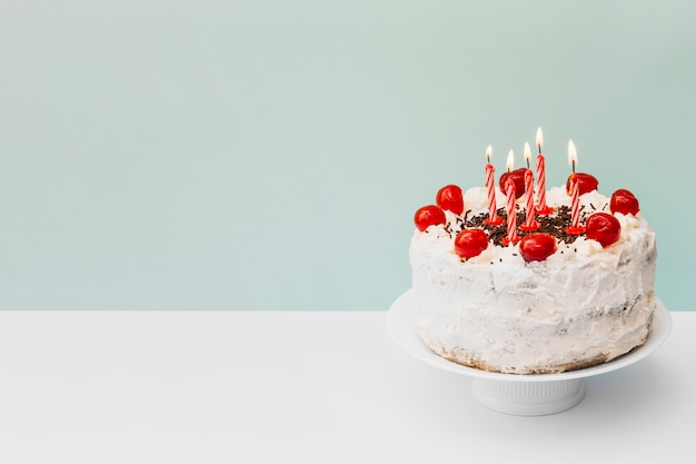 Illuminated candles on birthday cake on cake stand against blue background