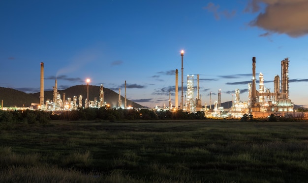 Illuminated factory by field against blue sky