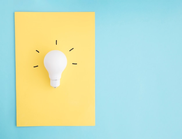 Illuminated white light bulb on yellow paper over the blue background