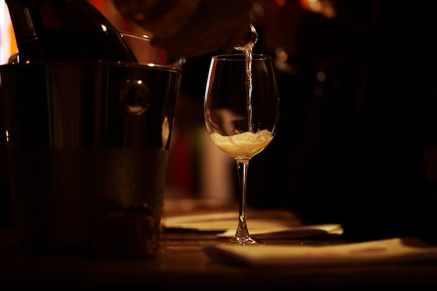 The illuminated wine glass stands on the table and a trickle of pink champagne is poured into it.