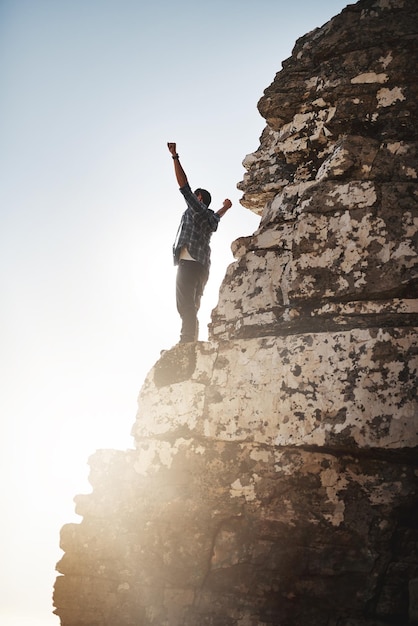 Im king of the world Shot of a young man standing on a mountain cliff with his arms raised