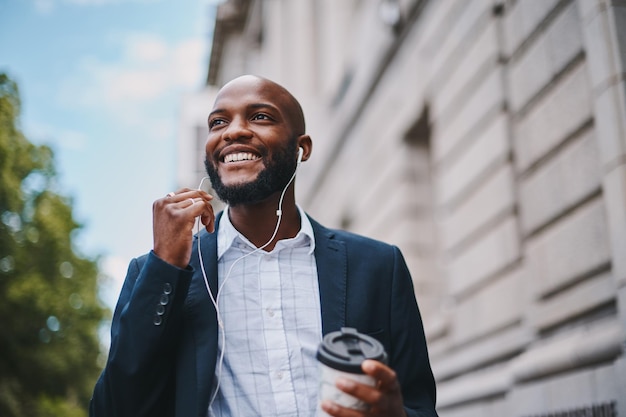 Im listening to my favourite motivational speaker Shot of a businessman holding a coffee and listening to music through earphones while walking through the city