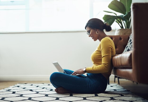 Im more productive when sitting on the floor Full length shot of an attractive young woman sitting alone at home and using her laptop