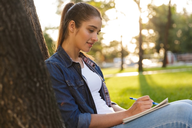 Image of amazing beautiful young woman student in the park writing notes.