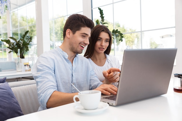 Image of amazing young loving couple sitting in cafe using laptop computer.