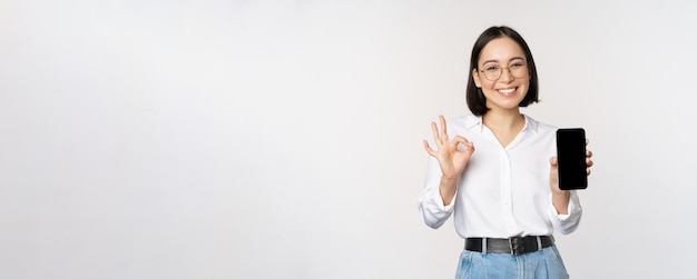 Image of asian businesswoman showing smartphone screen app interface and ok sign recommending applic