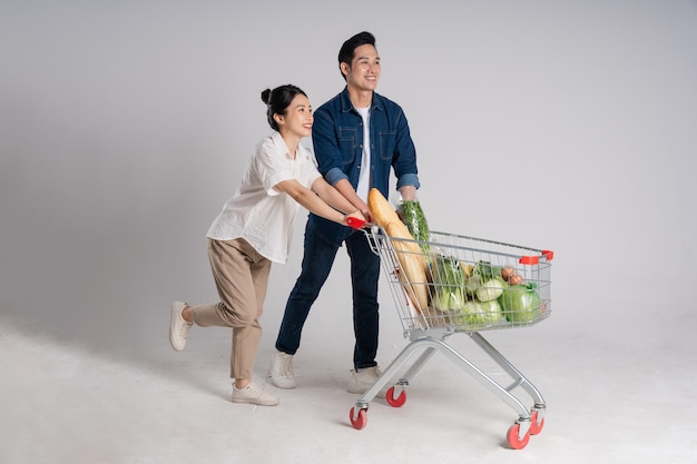 Image of Asian couple pushing supermarket cart while shopping isolated on white background