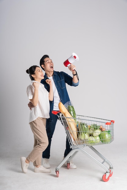 Image of Asian couple pushing supermarket cart while shopping isolated on white background