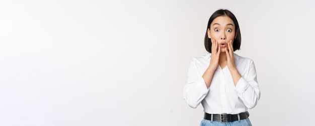 Image of asian female model looking surprised staring amazed reacting at surprise big news standing over white background