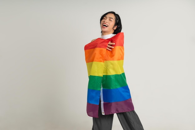 Image of Asian gay man holding a rainbow flag confidently posing on a white background