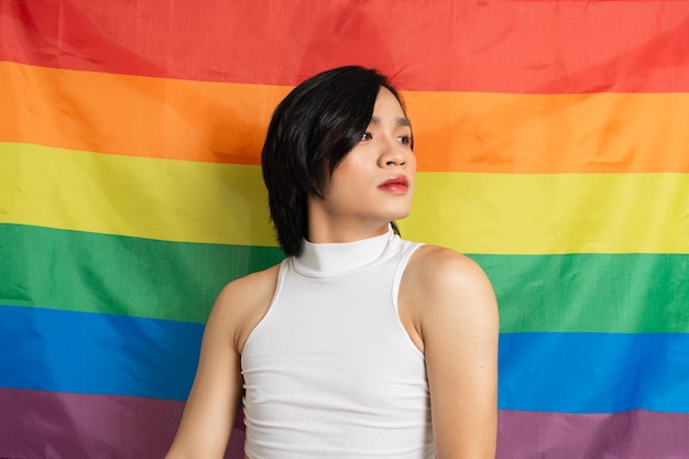 Image of Asian gay man holding a rainbow flag confidently posing on a white background