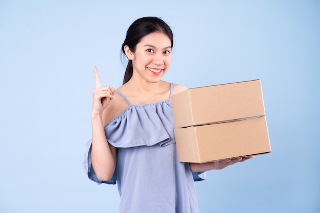 Image of asian girl holding a box, isolated on blue background