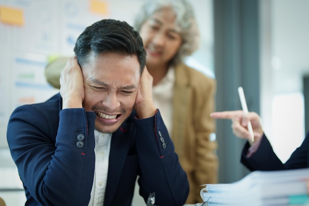 An image of an Asian male employee looking worried and sad about being scolded by his boss for failing to meet sales targets concept of disappointment and failure in his career