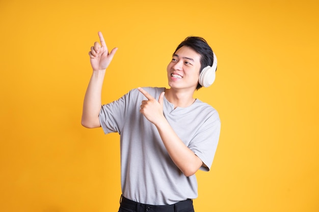 Image of asian man listening to music with headphones isolated on yellow background