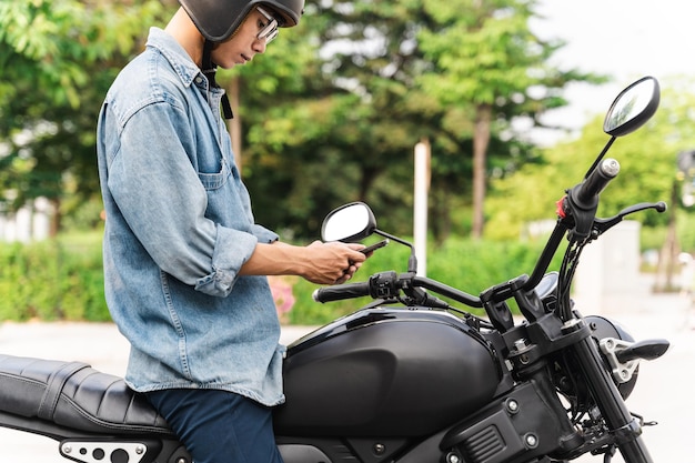 Image of asian man sitting on moto using mobile phone