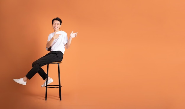 Image of asian man sitting on a stool isolated on orange background