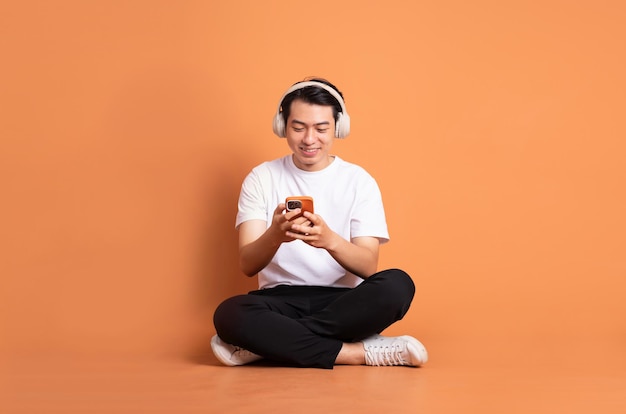 Image of asian man sitting using phone and isolated on orange background