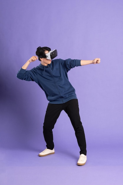 Image of asian man wearing virtual reality glasses on purple background