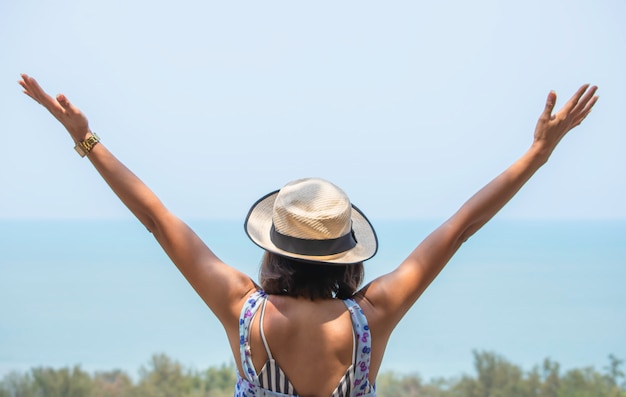 The image behind Asian women raise their arms and wear a hat  background sea.