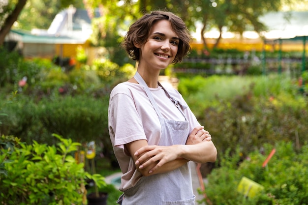 Image of attractive cute woman gardener standing over flowers plants in greenhouse