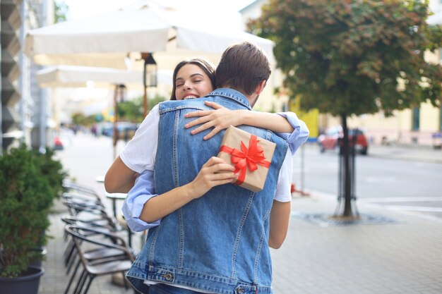 Image of attractive woman with present box giving hug to her man.