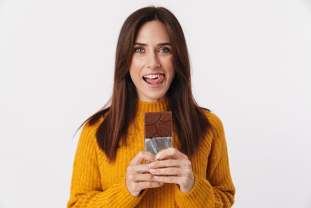 Image of beautiful brunette adult woman smiling and holding chocolate bar isolated on white