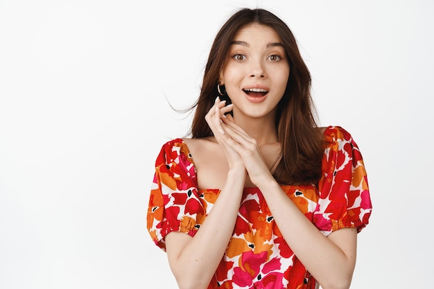 Image of beautiful girl looking excited in awe gazing with amazement and anticipation standing in floral dress over white background