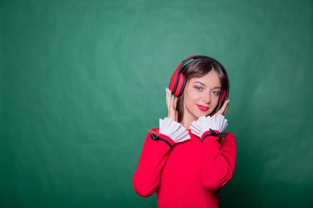 Image of beautiful girl in red dress listening to music isolated on green backgroundyoung smiling woman wearing wireless headphones listening a music and singingCopy space