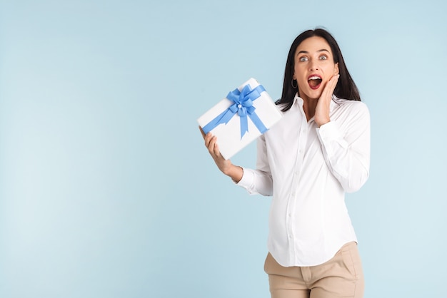 Image of a beautiful shocked young pregnant woman isolated holding gift box.