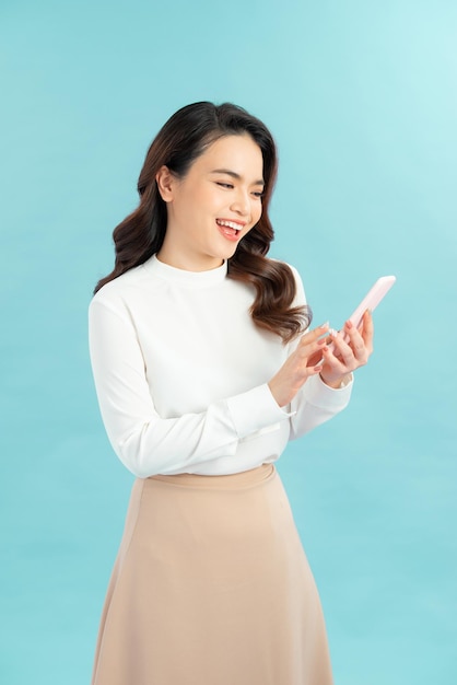 Image of a beautiful thinking young woman posing isolated over blue wall background using mobile phone