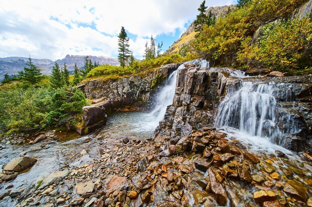 Image of Beautiful waterfalls over tiers of gray and brown rocks with view of open valley and mountains