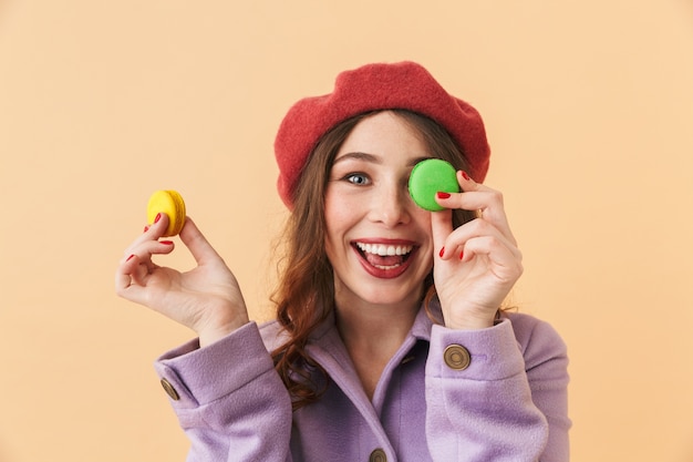 Image of beautiful woman 20s with long hair smiling and holding macaroon cookies, standing isolated 