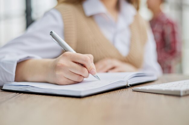 Image beautiful woman writing down notes while sitting at table in office