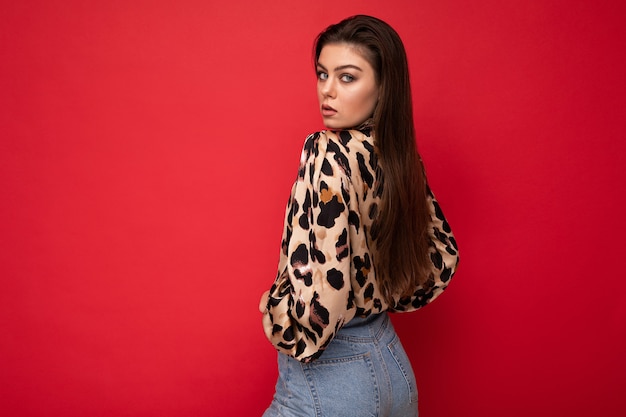 Image of a beautiful young brunette woman dressed in animal printed blouse posing isolated over red