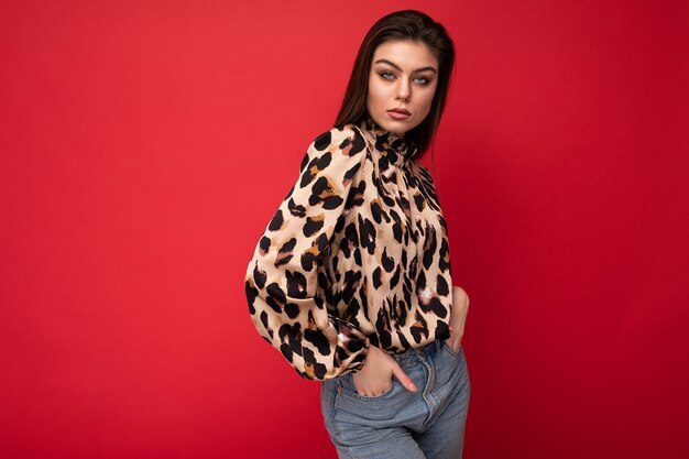 Photo image of a beautiful young brunette woman dressed in animal printed blouse posing isolated over red