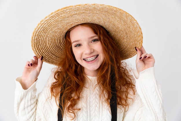 Image of a beautiful young cute girl redhead posing isolated over white wall background wearing hat.